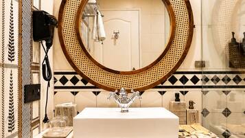 A bathroom with a round mirror, white sink, and wooden cabinet with a woven front panel.