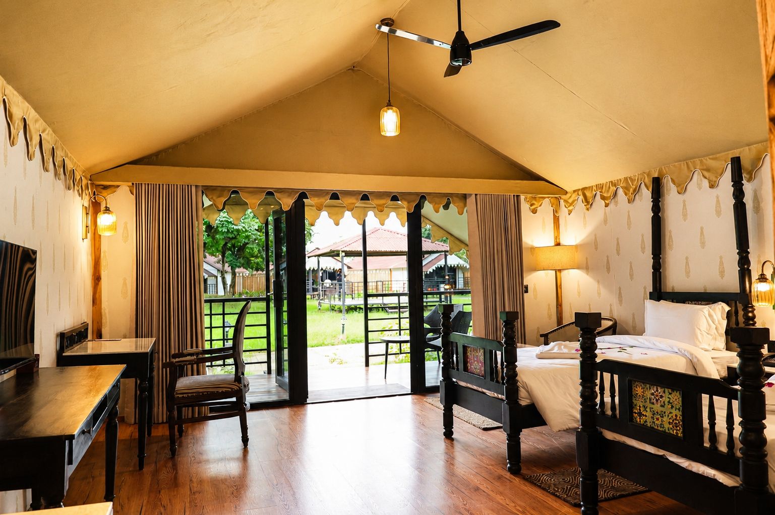 A room with a bed, a desk, a chair, a ceiling fan, and a view of the outdoors.