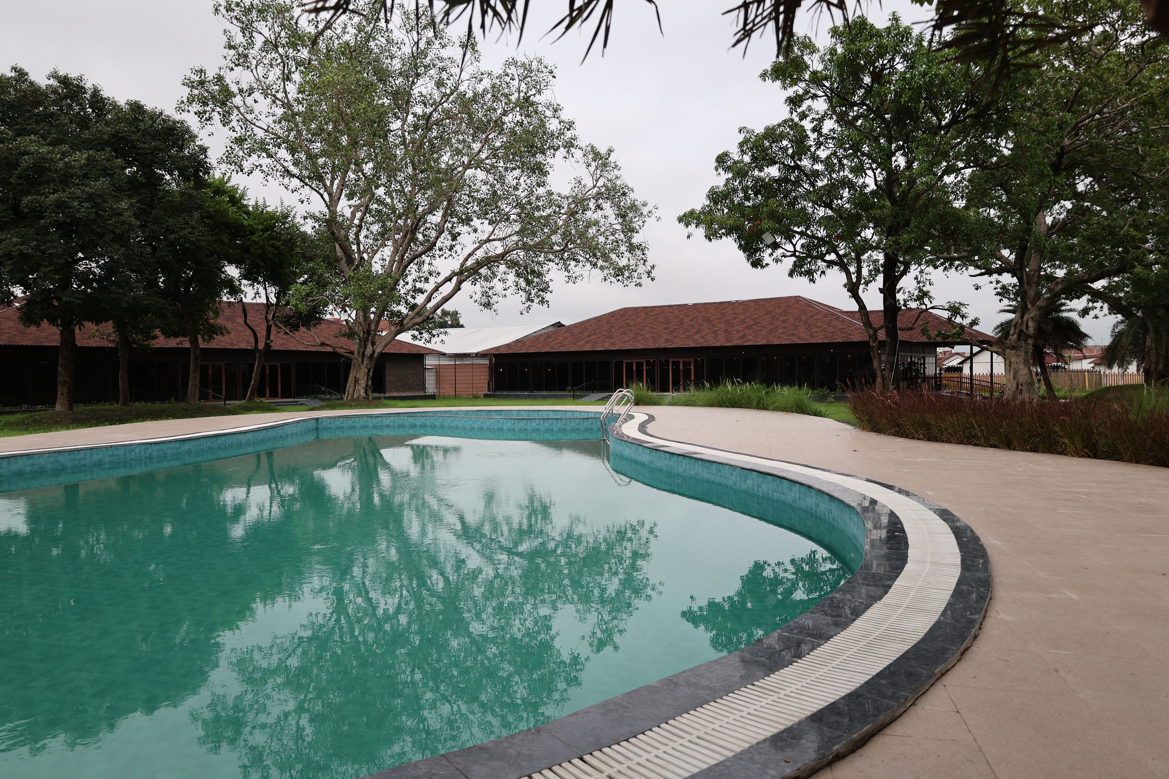 A swimming pool with a curved edge, surrounded by trees and a building with a tiled roof.