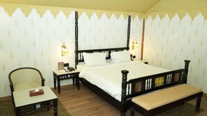 Een slaapkamer met een hemelbed, bedlampjes, een stoel, een klein tafeltje en een bankje.