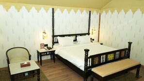 A bedroom with a four-poster bed, bedside lamps, a chair, a small table, and a bench. - Evoke Rambagh Ayodhya (Faizabad)
