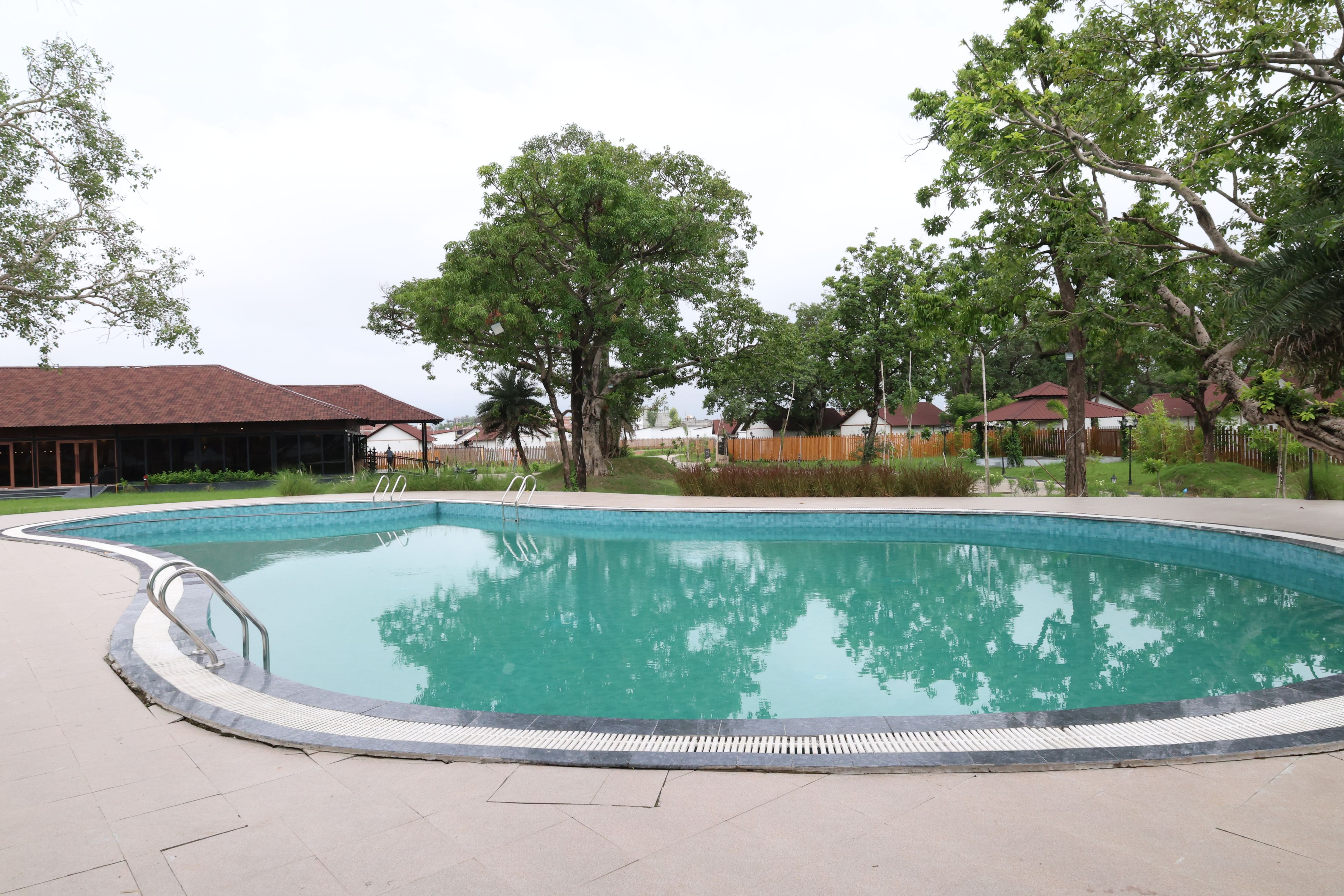 A swimming pool with a tiled deck, surrounded by trees and buildings.