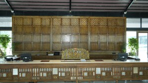 Uma mesa de recepção com um painel decorativo, área de recepção e plantas em vasos.