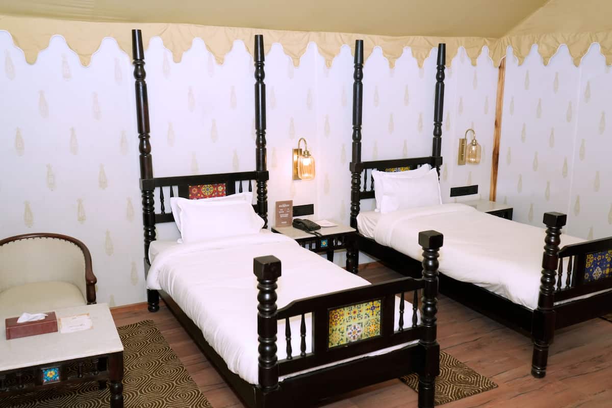 A hotel room with two wooden beds, a chair, a small table, and a decorative wall panel.