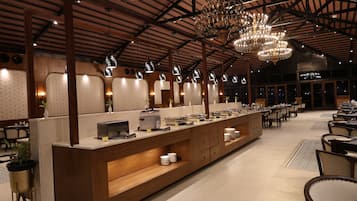 Un hall d’hôtel spacieux, doté d’un long comptoir de réception, de nombreuses tables et d’un plafond haut orné de lustres.