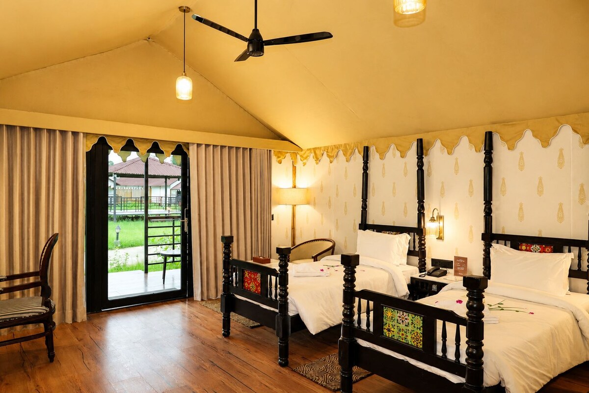 Une chambre d’hôtel avec un grand lit, une chaise, un ventilateur de plafond et une vue sur un jardin, accessible par une porte vitrée.
