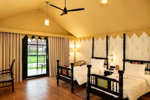 A hotel room with a large bed, a chair, a ceiling fan, and a view of a garden through a glass door.