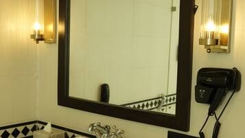 A bathroom with a large mirror, a white sink, two wall-mounted lights, a towel dispenser, and a soap dispenser.