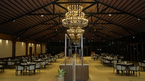 Ein großzügiger Bankettsaal mit hohen Decken, einer zentralen Chandelier und mehreren für das Servieren angerichteten Esstischen.
