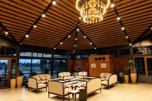 A spacious indoor area with multiple seating arrangements, a large chandelier, and large windows offering views of the outside.
