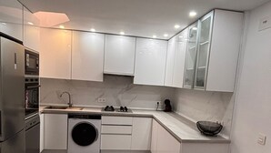 A modern kitchen with white cabinets, a built-in washing machine, a stainless steel refrigerator, and a microwave.