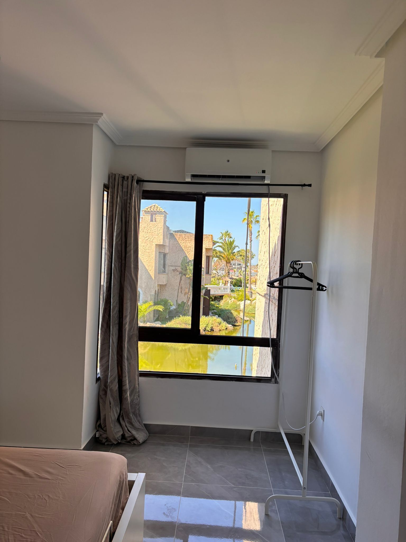 Een kamer met een groot raam, een bed, een kledingkast en een airconditioning.