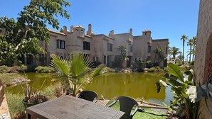 A patio with a table and chairs, a small pond, and a building with multiple windows and balconies in the background.