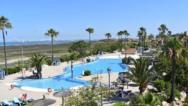 A resort with a large swimming pool surrounded by palm trees and beach chairs.