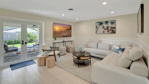 A modern living room with a white sofa, a coffee table, and a painting of a sunset. - 702B |Delray/Chapel Hill |Heated Pool |Putting Green |Fire Pit |by DelrayNightly (Boynton Beach)