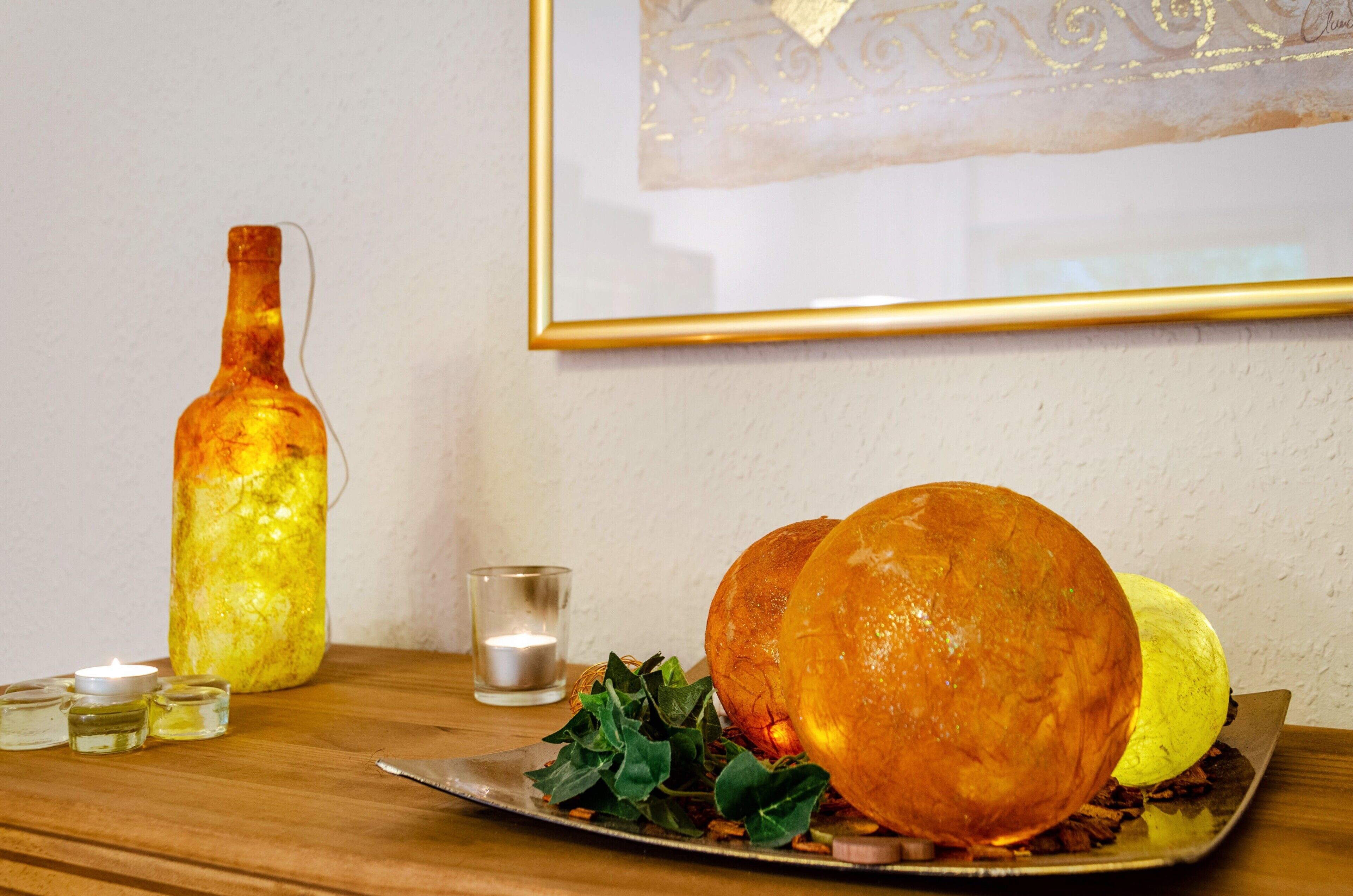 Een tafel met kaarslicht, een decoratieve glazen fles, een ingelijste afbeelding en een bord met een groot broodje.