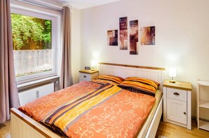 Een slaapkamer met een bed, twee nachtkastjes, een radiator en een raam met gordijnen.