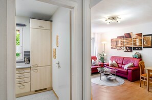 A room with a red sofa, a coffee table, and a dining table. There is a kitchen area with cabinets and a refrigerator.