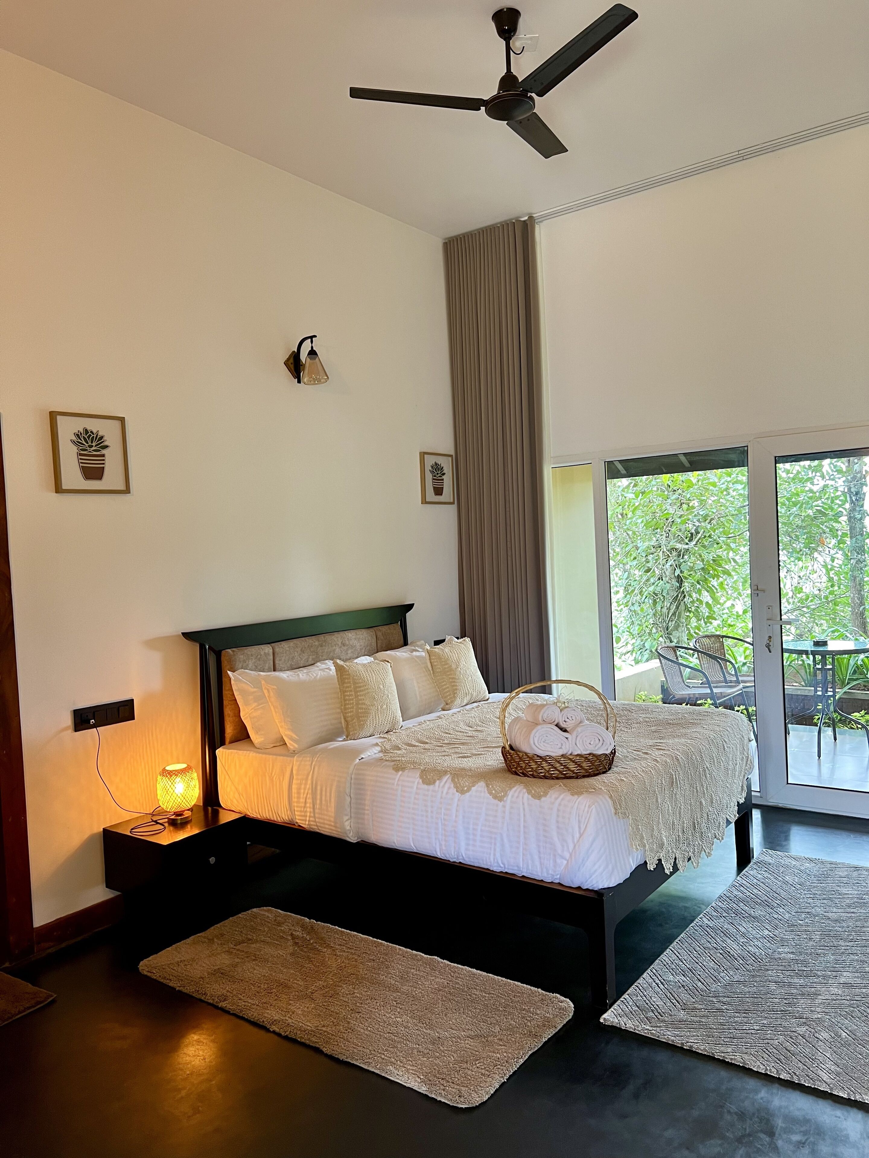 Une chambre moderne avec un grand lit, un ventilateur de plafond et une vue sur l’extérieur grâce à une porte-fenêtre coulissante.