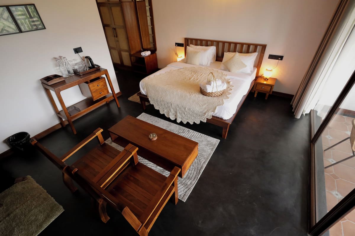 A bedroom with a large bed, bedside tables, a wooden desk, and a view through a window.