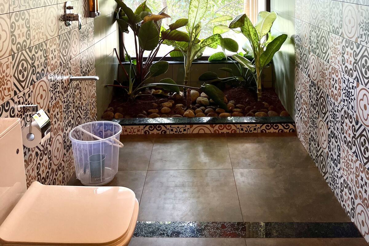 A bathroom with patterned tiles, a toilet, a sink, and a window with a view of trees.