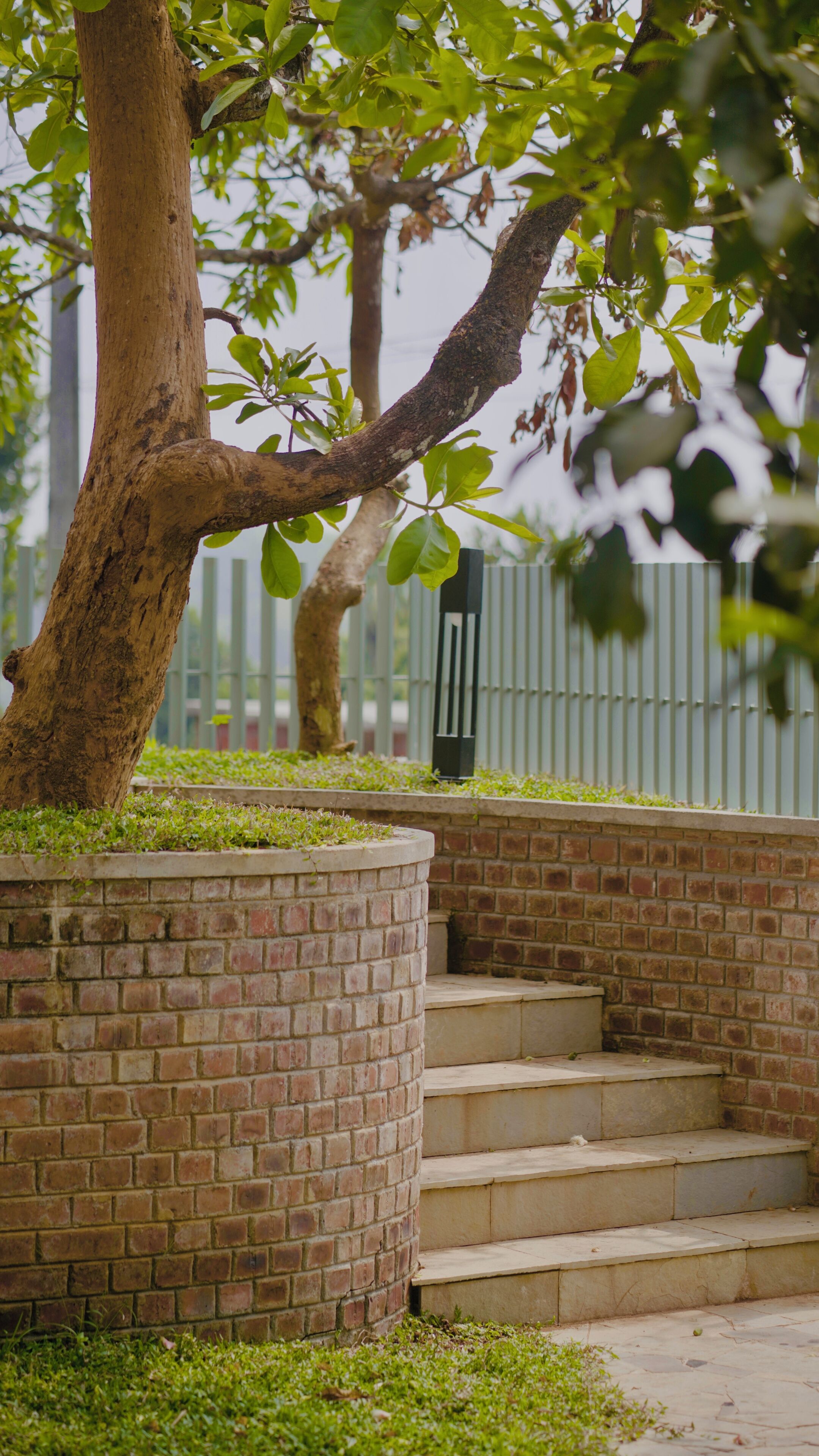 A brick staircase with a metal railing, surrounded by greenery and a fence.
