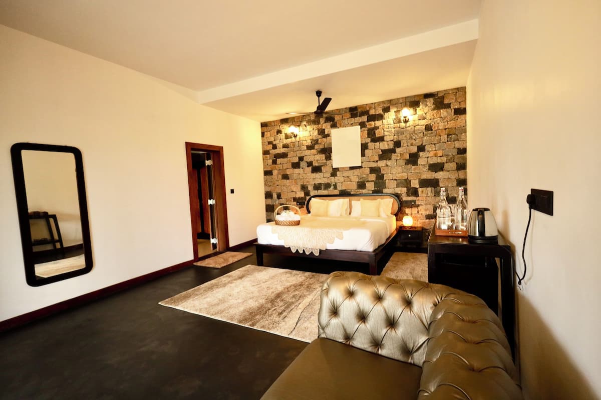 A bedroom with a stone wall, a bed, a bedside table, a mirror, and a leather chair.