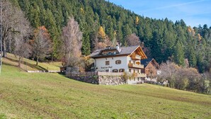 A chalet-style building with a stone foundation, wooden balconies, and a mountain backdrop. - Apartment 'Ifinger' with Mountain View, Shared Garden and Wi-Fi (Avelengo)