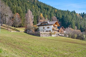 Un edificio de estilo chalé con base de piedra, balcones de madera y montañas al fondo.