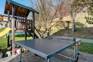 A ping pong table in an outdoor setting with a wooden structure and a playground in the background.