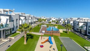 Um complexo residencial moderno com parquinho, piscina e jardins bem cuidados.