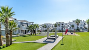 Um bairro residencial moderno com gramado bem cuidado, palmeiras e um parquinho.