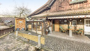 A rustic wooden building with a tiled roof, a wooden fence, and a brick patio with outdoor seating. - Apartment 'Hirtenhaus' with Shared Terrace and Wi-Fi (Attendorn)