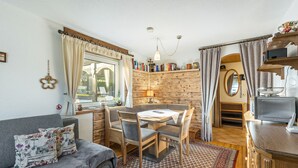 A cozy room with a sofa, a dining table with chairs, a bookshelf, a small kitchen area, and a window with curtains. - Apartment 'Hirtenhaus' with Shared Terrace and Wi-Fi (Attendorn)