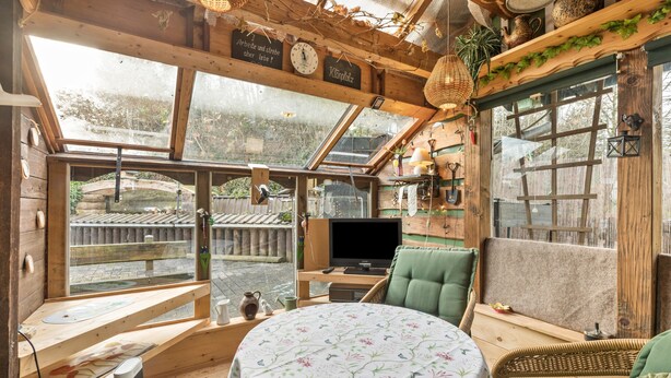A cozy room with a wooden interior, a round table with a floral tablecloth, a green cushioned chair, and a television. - Apartment 'Hirtenhaus' with Shared Terrace and Wi-Fi (Attendorn)