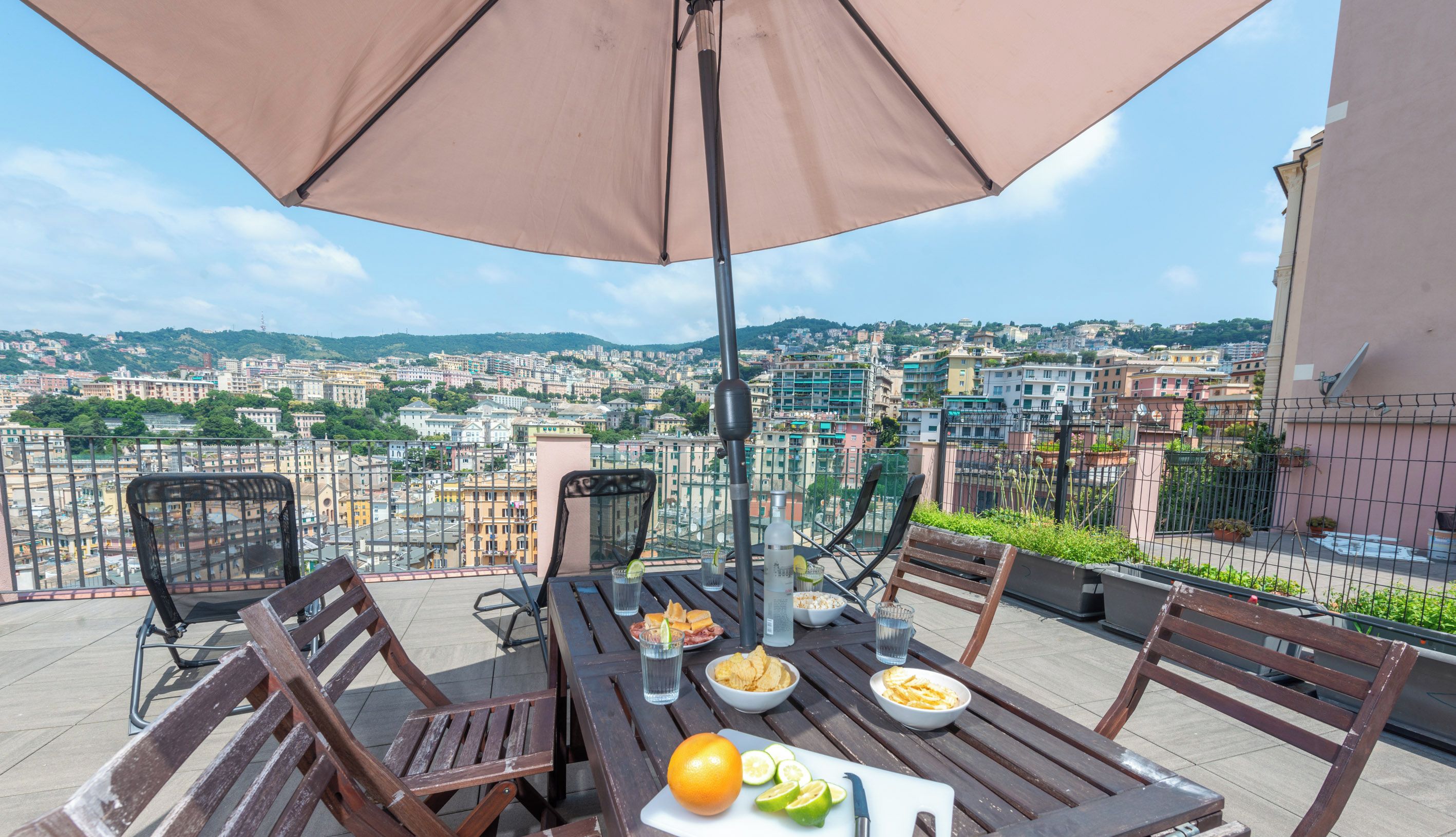 Une terrasse avec une table dressée pour le dîner, un grand parasol et une vue sur la ville en arrière-plan.