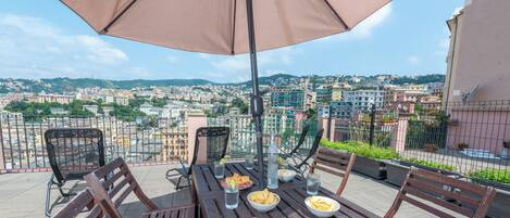 Une terrasse avec une table dressée pour le dîner, un grand parasol et une vue sur la ville en arrière-plan.
