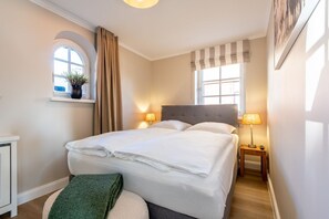Un lit bien fait, avec du linge de lit blanc, une table de chevet avec une lampe, une fenêtre avec des rideaux et une petite plante posée sur le rebord de la fenêtre.