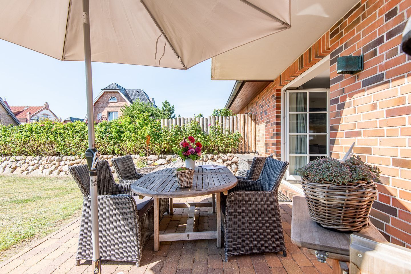 A patio with a round table and wicker chairs, a potted plant, and a brick wall.