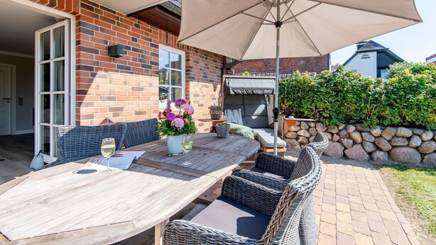 An outdoor patio with a wooden table, wicker chairs, and a large umbrella. - Käpt'n 25 - Käpt'n 25 Westerland (Sylt)