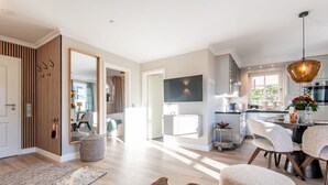 A spacious living area with a large TV, a dining area with a chandelier, and a kitchen with modern appliances. - Käpt'n 25 - Käpt'n 25 Westerland (Sylt)
