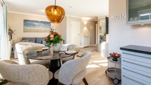 A modern dining area with a round table, grey upholstered chairs, a hanging pendant light, and a vase of flowers. - Käpt'n 25 - Käpt'n 25 Westerland (Sylt)