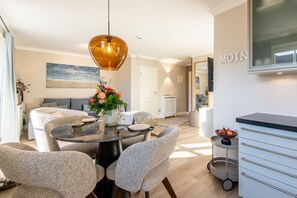 Un espace repas moderne avec une table ronde, des chaises à revêtement gris, un luminaire suspendu et un vase de fleurs.
