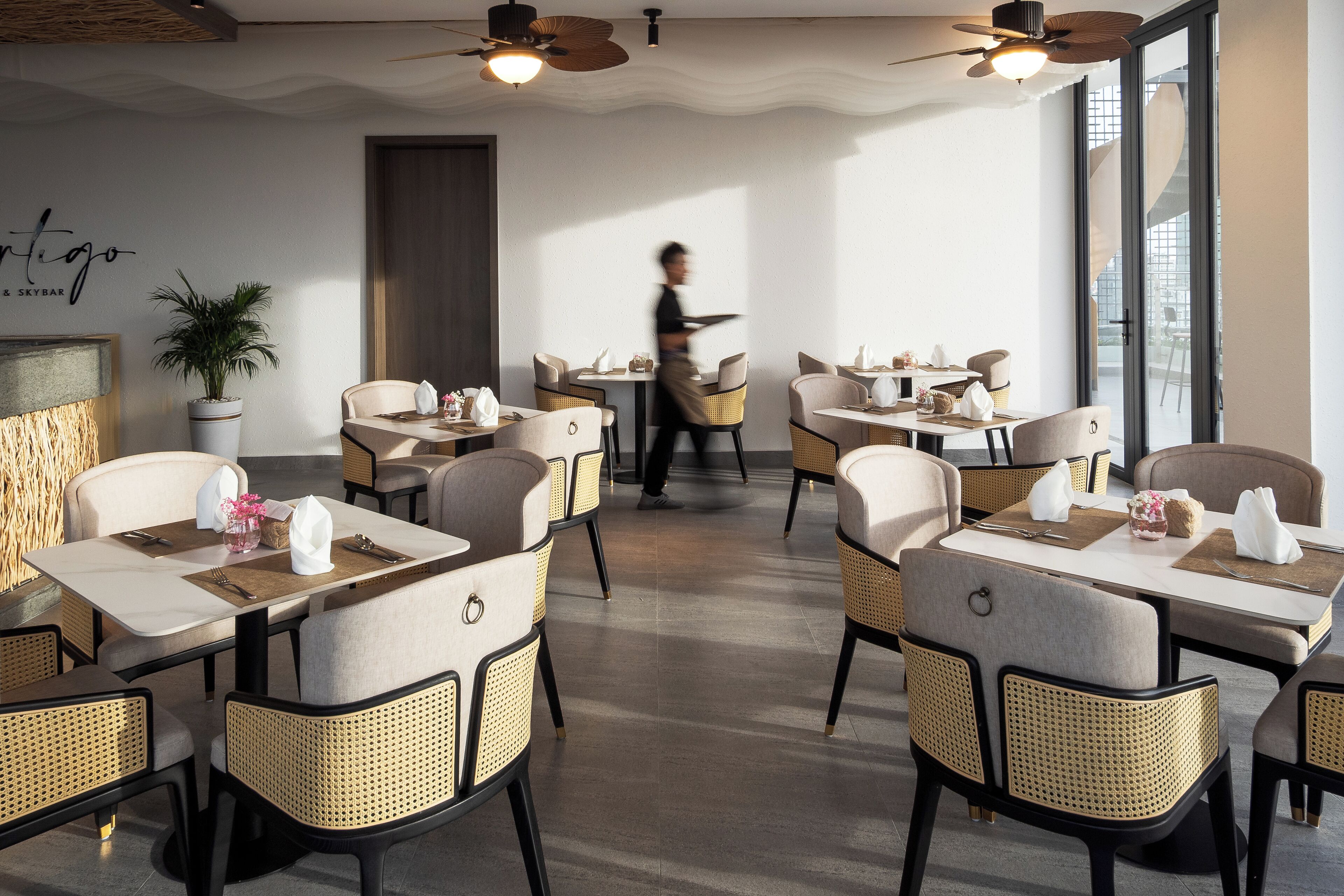 Un espace repas moderne avec des tables rondes, des chaises en osier et des ventilateurs de plafond.