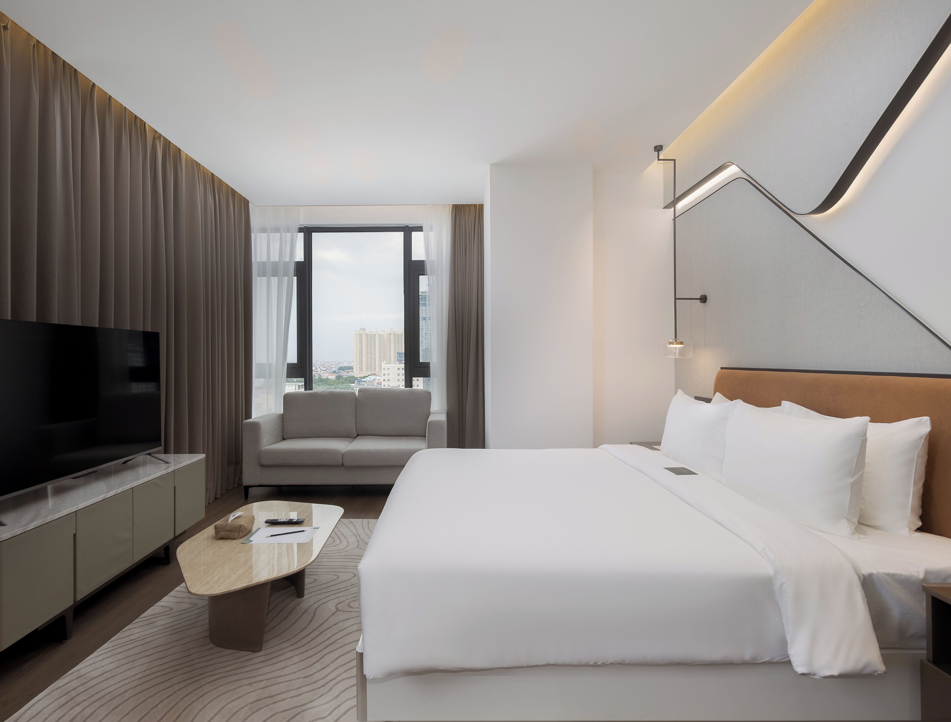 A modern hotel room with a large bed, a TV, a sofa, and a desk.