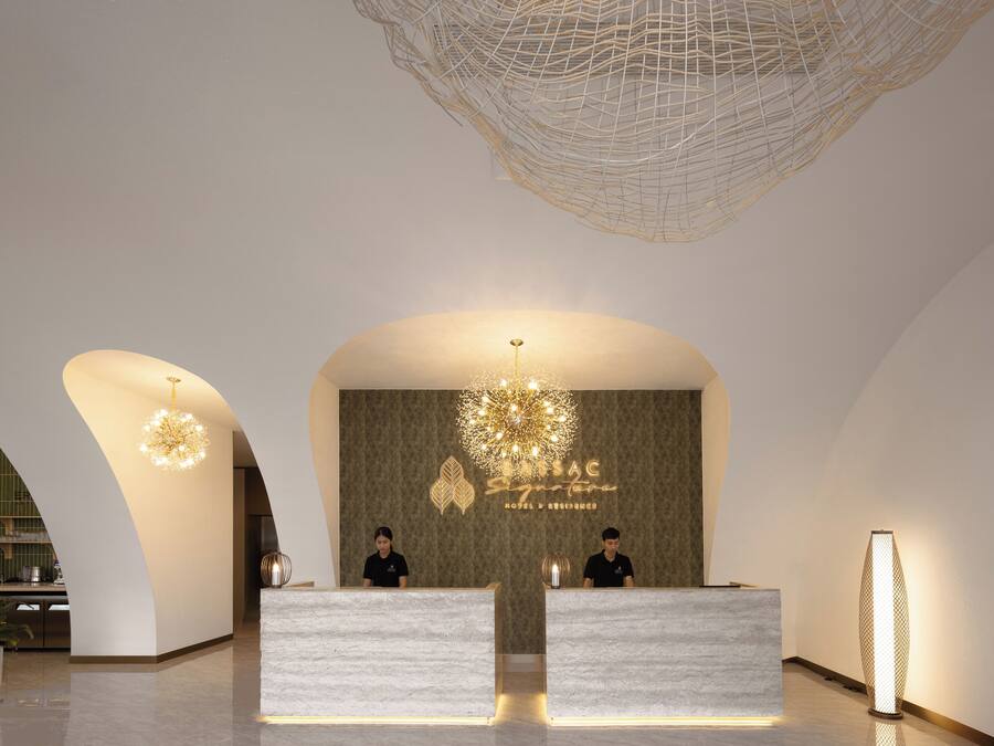 A modern hotel reception area with two receptionists, a decorative chandelier, and a reception desk.