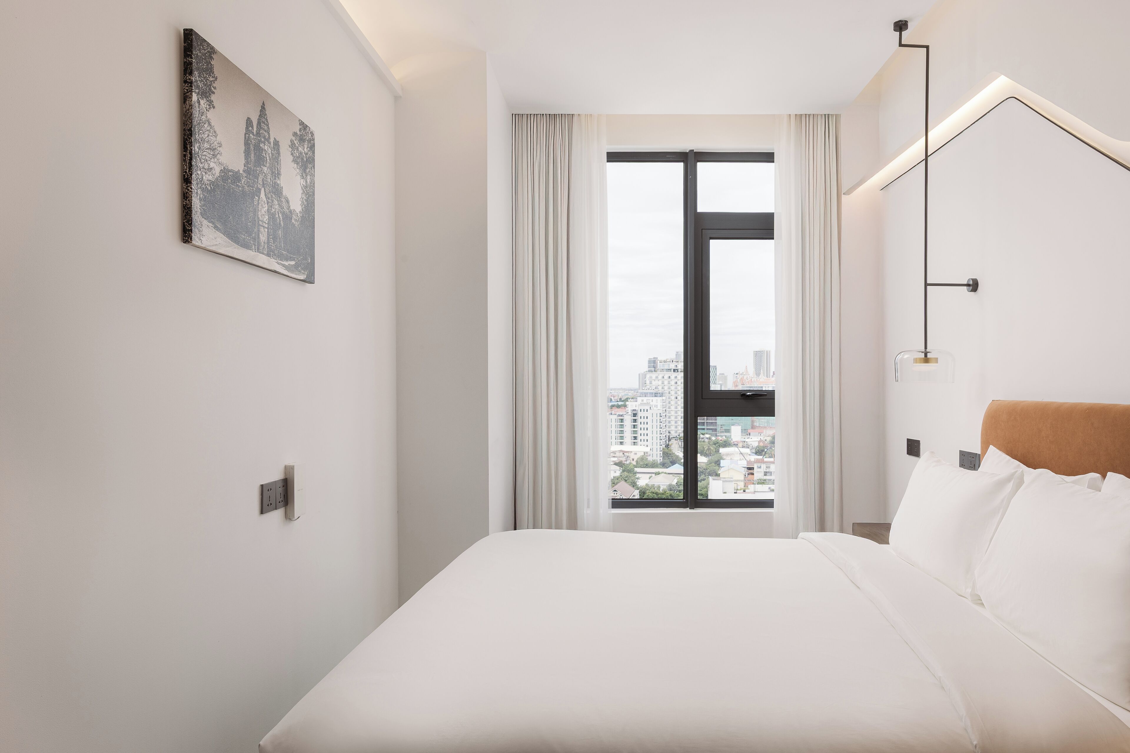 A hotel room with a large window, a bed, a nightstand, and a wall-mounted lamp.