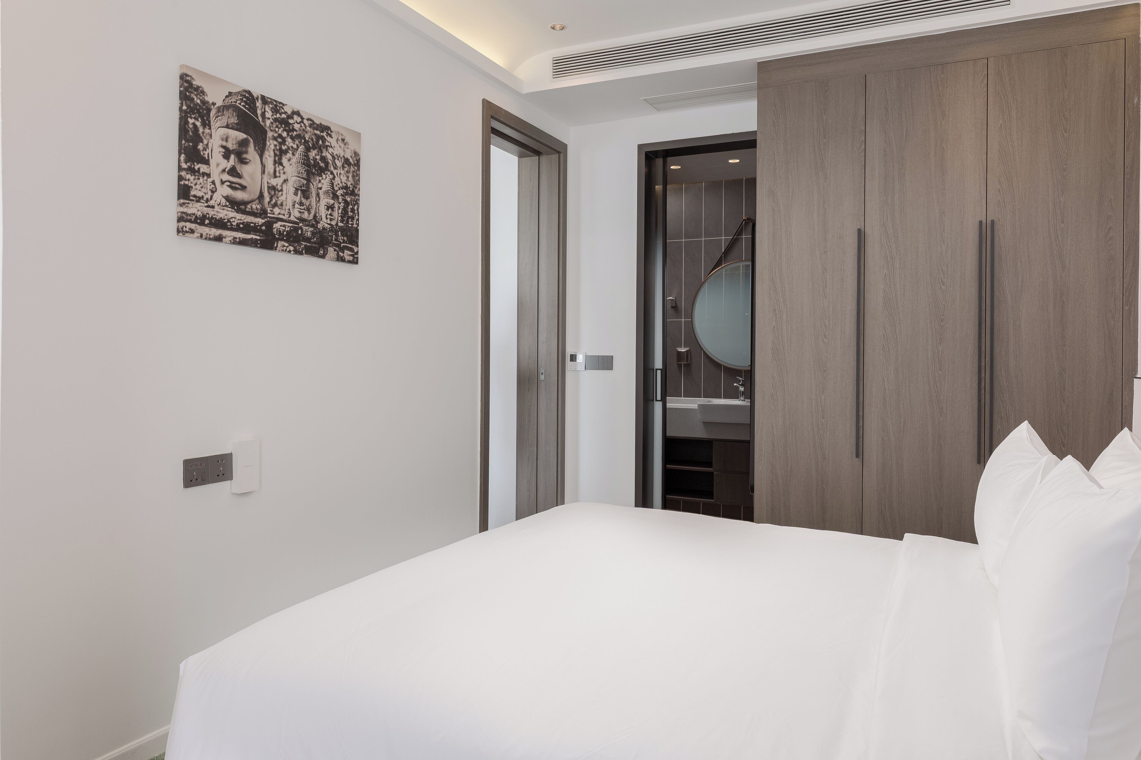 A modern hotel room with a bed, a wardrobe, a mirror, and a wall-mounted artwork.
