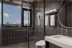 Un baño moderno con ducha de vidrio, inodoro, lavamanos y un espejo grande.