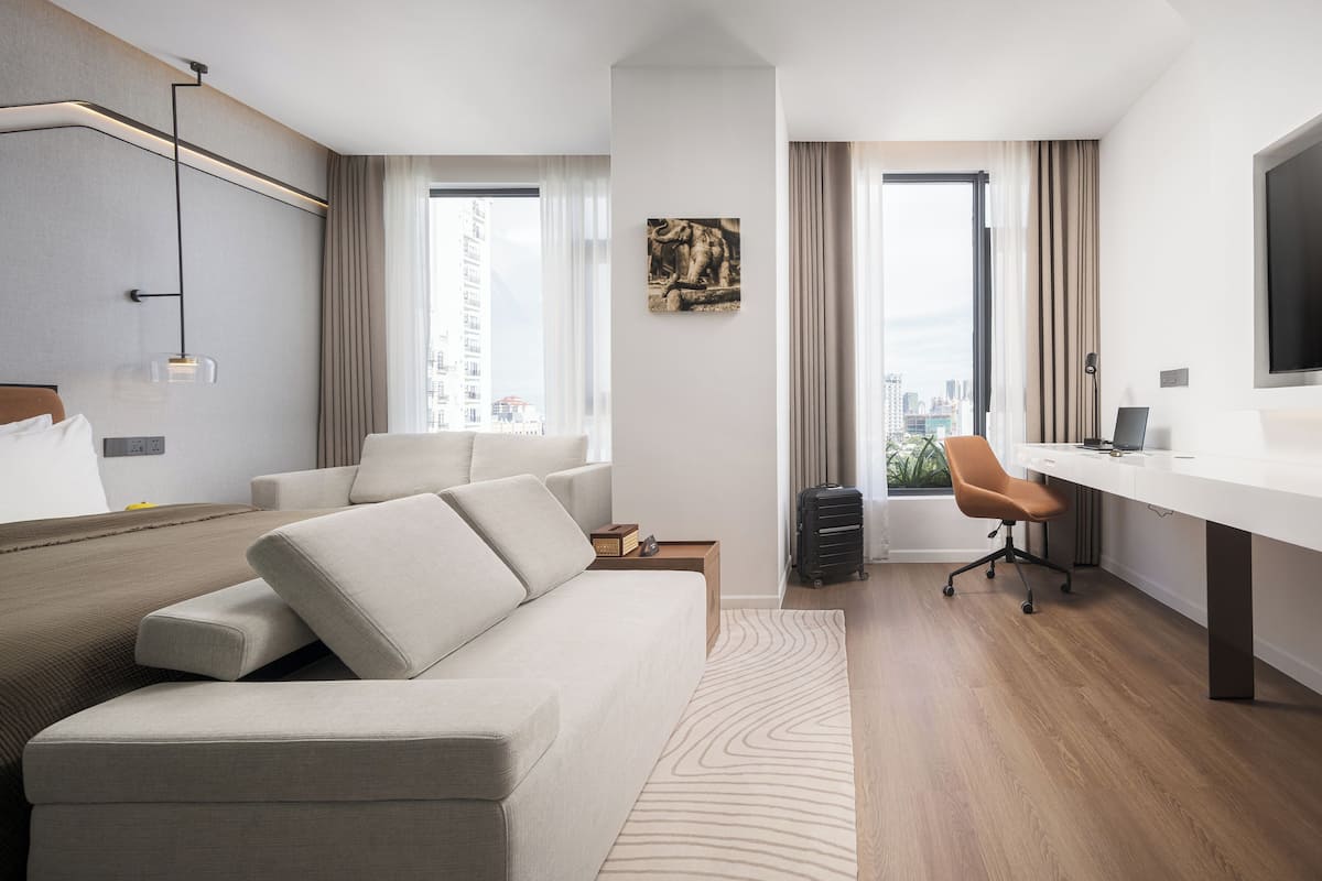 Quarto de hotel moderno com sofá, escrivaninha, cadeira e uma grande janela com vista para a cidade.